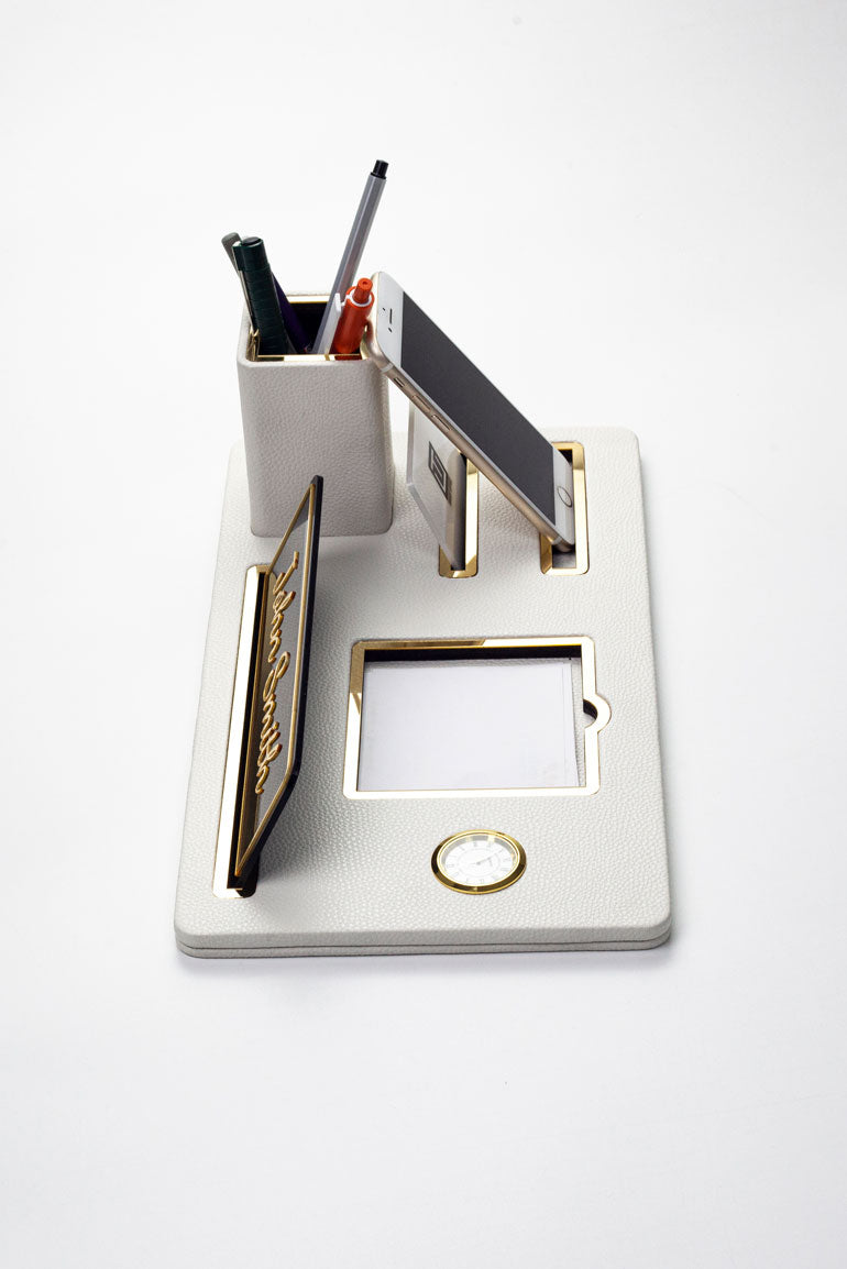 لوحة اسم مكتبية من الجلد، منظم مكتب، ساعة ذهبية بيضاء مزينة بتفاصيل، حامل أقلام.