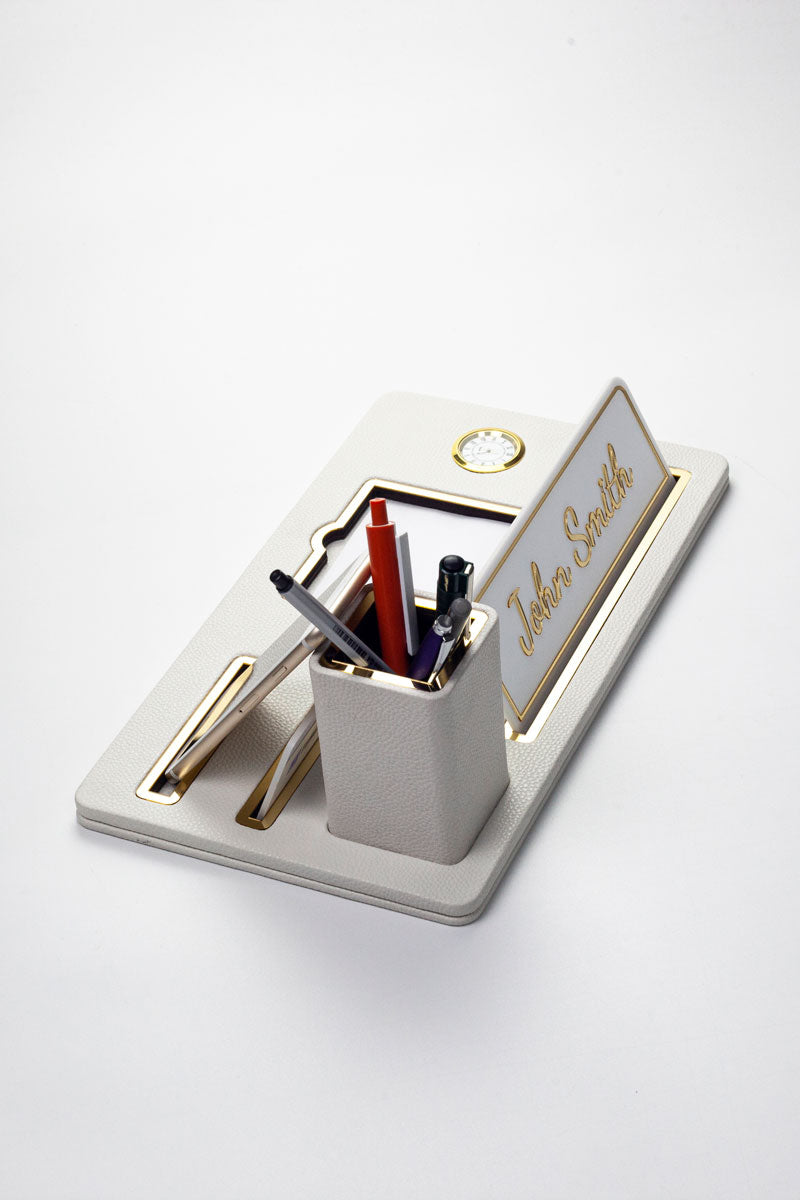 لوحة اسم مكتبية من الجلد، منظم مكتب، ساعة ذهبية بيضاء مزينة بتفاصيل، حامل أقلام.